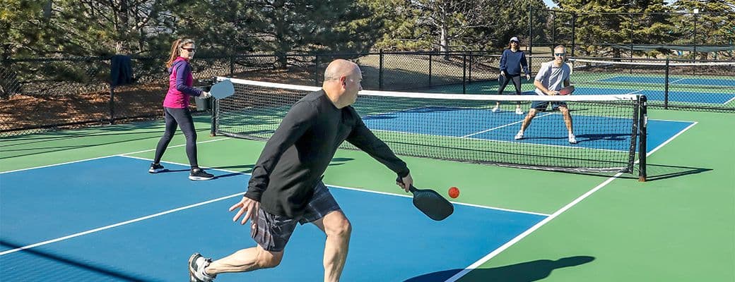 Four adults playing pickleball on an outdoor court on a sunny day